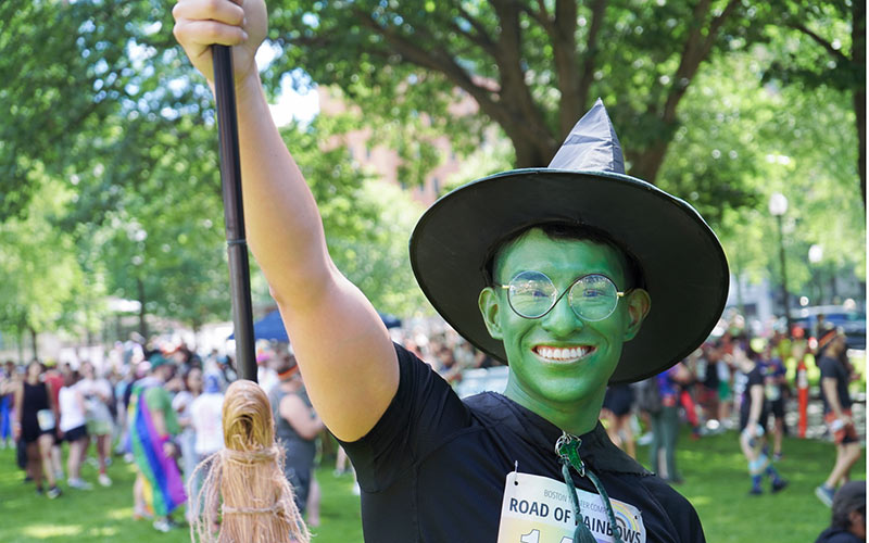 Adilson Gonzalez wearing a green halloween costume. Costume is made from thrifted items to create a wicked inspired outfit. Person wear green makeup, infinity glasses, a cape with a green brooch, and a black pointy hat.