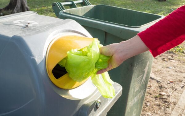 a woman puts a plastic bag into a recycling bin.