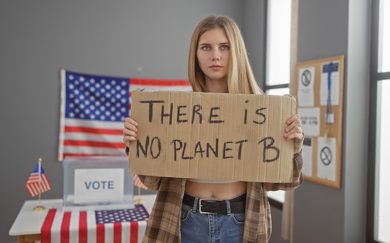 A young woman holding a protest sign 'there is no planet b' stands in a usa voting center, symbolizing environmental activism.