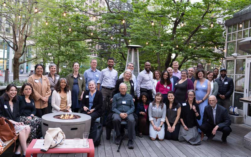 Group of members, pro-bono volunteers, and leaders of the Environmental Justice Assistance Network (EJAN) gathered outside on a deck with trees on the background for re-launch celebration event.