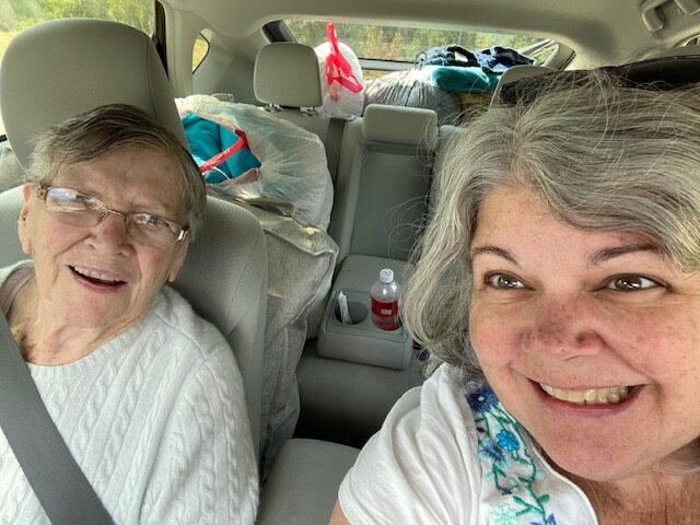 two women in car with trash bags filled with clothes in the back seat