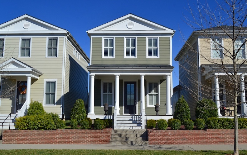 Olive green New England colonial house in a neighborhood of similar homes.